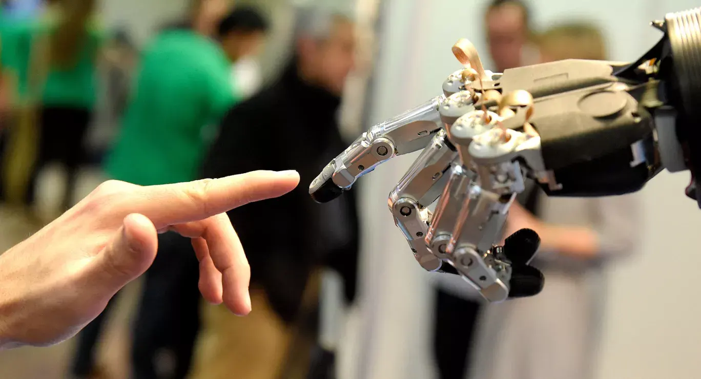 A robotic hand reaching out to touch a human finger, symbolising the connection between technology and humanity.